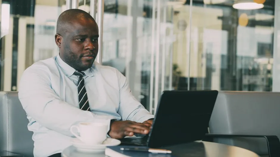 Businessman in cafe working on laptop with cup of coffee.